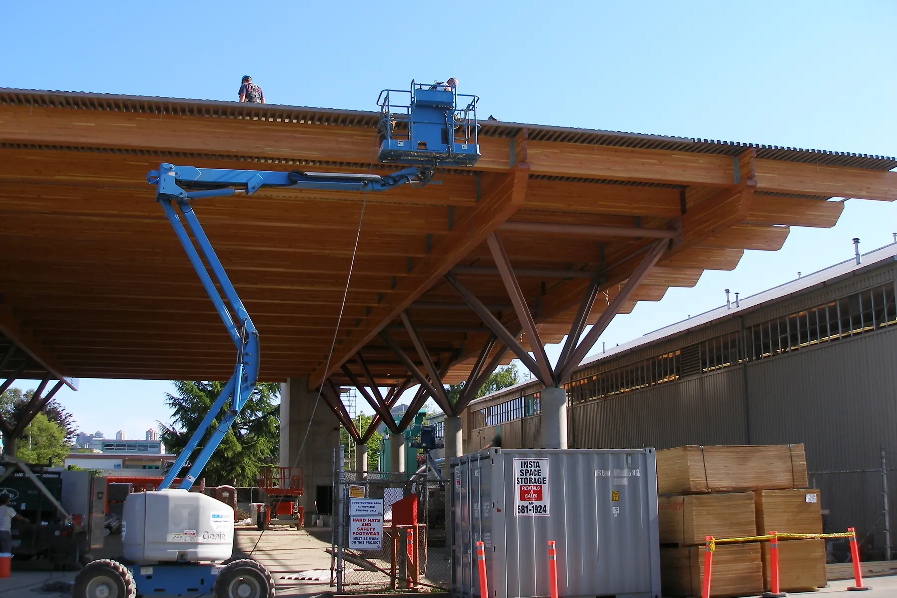 Workers on a boom lift and the roof deck finish a large glulam timber canopy under construction at BCIT in Burnaby, British Columbia