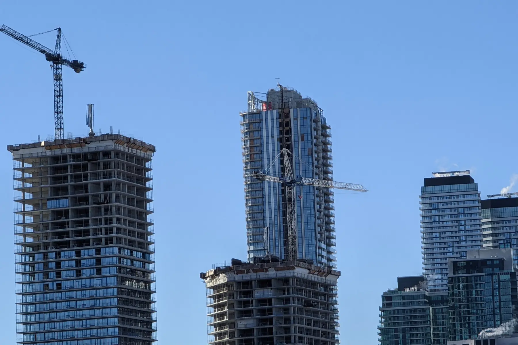 High-rise towers under construction with tower cranes against a blue sky in Toronto